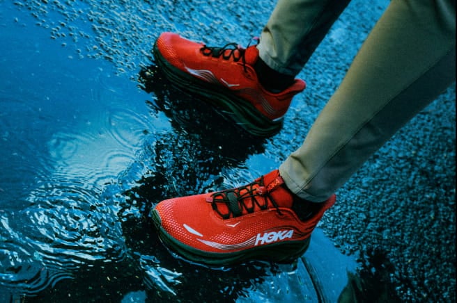Gros plan d’une personne debout dans l’eau boueuse en chaussures HOKA.